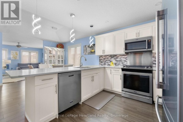 Modern kitchen with white cabinets, stainless steel appliances, and pendant lighting. - 8 Windward Way N, Ashfield Colborne Wawanosh