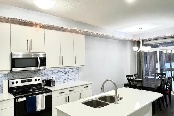 Kitchen island with sink, dining area with black table and chairs, and sliding doors. - 80 - 1375 Whetherfield Street, London North