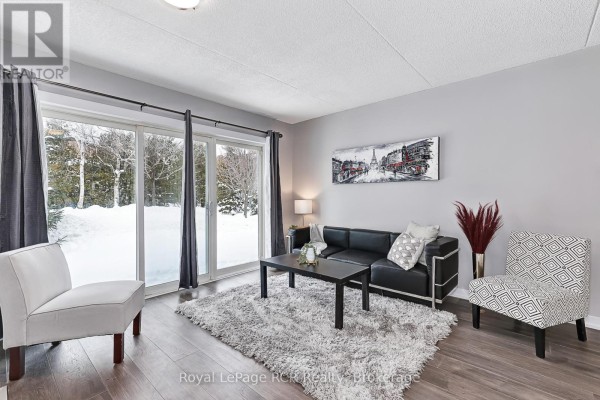 Open concept living area with kitchen, fireplace, and entrance door, featuring grey walls and wood flooring. - 80 - 21 Dawson Drive, Collingwood