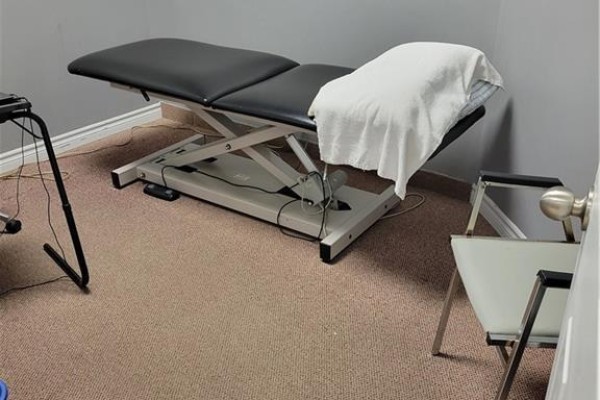 Adjustable examination table with black upholstery on a carpeted floor. - 80 Hamilton Street N Unit# 5, Waterdown