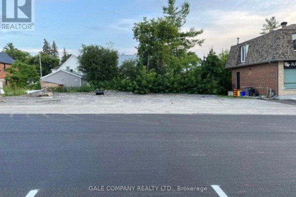 Empty paved lot with gravel at the rear, flanked by trees and buildings. - 80 High Street, Mississippi Mills