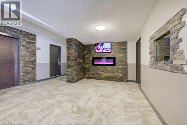 Apartment building hallway with stone accent wall, electric fireplace, and mounted television. - 80 King Edward Avenue Unit# 409, London