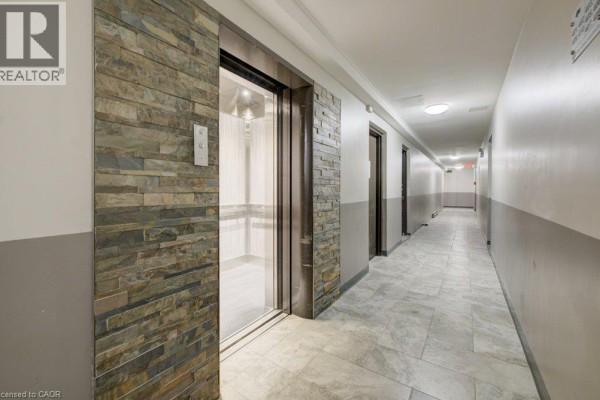 Apartment building hallway with glass elevator, stone accent wall, and multiple doors. - 80 King Edward Avenue Unit# 409, London