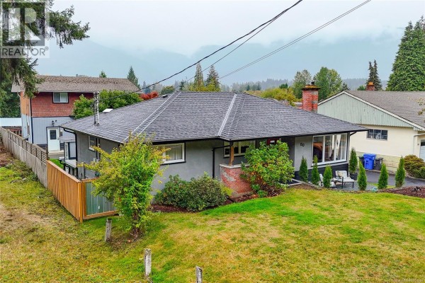 Front view of a grey bungalow with a dark roof, grey shingle siding, and a paved driveway. - 80 North Shore Rd, Lake Cowichan