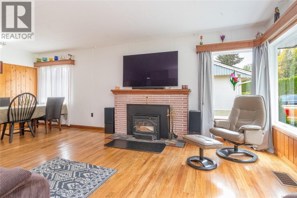 Living room with a brick fireplace, wood-burning insert, large television, and comfortable seating. - 80 North Shore Rd, Lake Cowichan