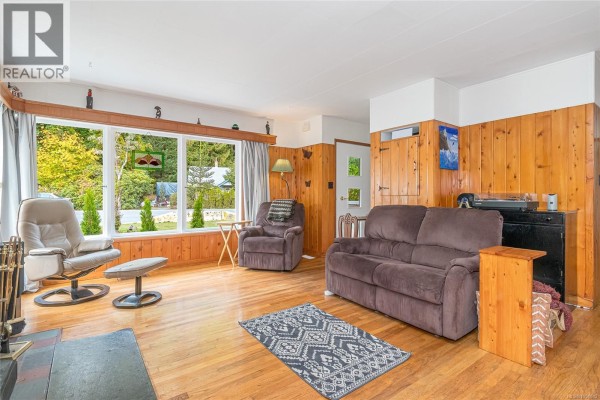 Living room with pine paneling, wood floors, a brown sofa, two armchairs, and a large window view. - 80 North Shore Rd, Lake Cowichan