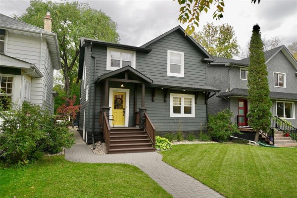 Front view of a dark grey house with a covered porch and a paved walkway. - 80 Tache Avenue, Winnipeg