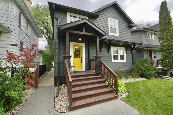 Close-up of the front entrance of a dark grey house with a yellow door and wooden steps. - 80 Tache Avenue, Winnipeg