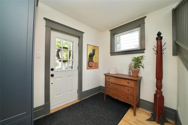 Entryway with a white door, dark grey trim, wooden dresser, and a black rug. - 80 Tache Avenue, Winnipeg