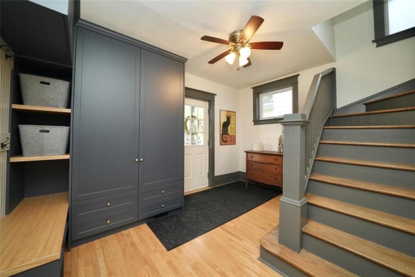 Interior entryway with a large grey cabinet, wooden floor, staircase, and ceiling fan. - 80 Tache Avenue, Winnipeg