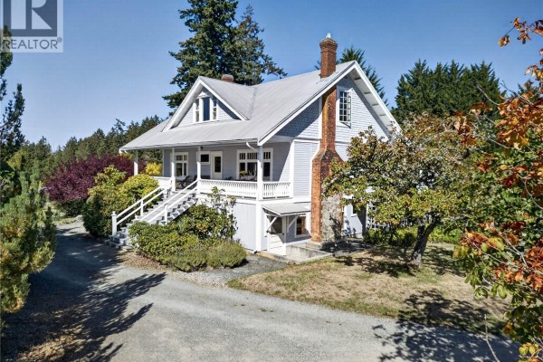 Light blue house with white trim, a brick chimney, and a wrap-around porch surrounded by trees. - 800 Lower Ganges Rd, Salt Spring