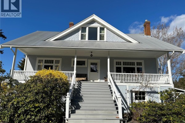 Front view of a light blue house with a large porch, stairs, and surrounding trees. - 800 Lower Ganges Rd, Salt Spring