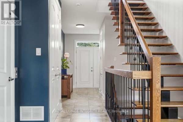 Interior view of a townhouse foyer with a wood staircase, blue accent wall, and front door. - 800 Petra Private, Ottawa