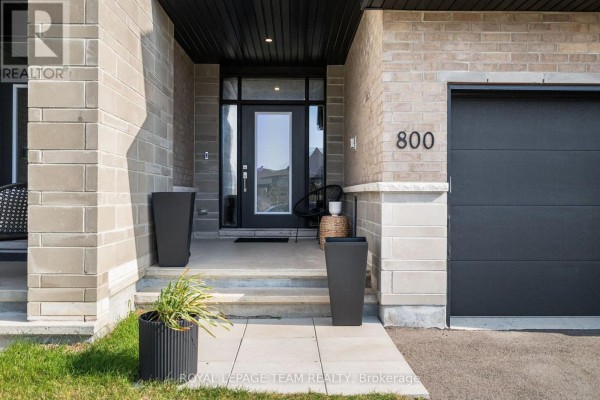 Front entrance with a black door, glass panels, and concrete steps with planters. - 800 Solarium Avenue, Ottawa