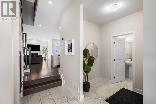 View from the entryway down a hall, showing dark wood stairs and access to the living area. - 800 Solarium Avenue, Ottawa