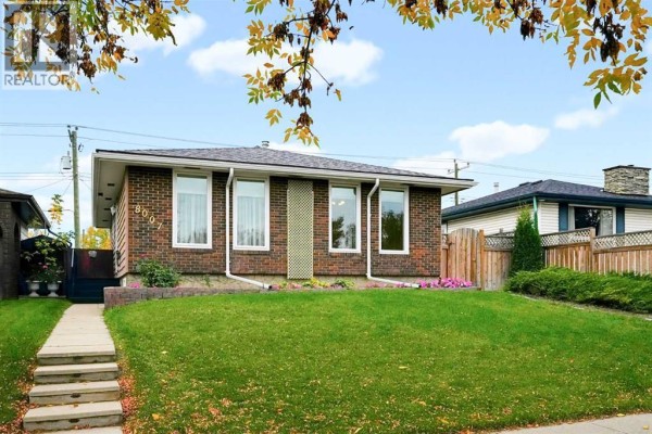 Front exterior of a red brick bungalow with a large green lawn and a wooden fence. - 8007 Huntington Street Ne, Calgary