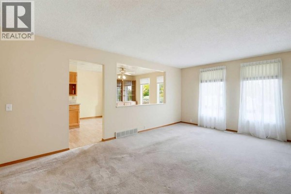 Living room showing an opening to the kitchen and dining area with two windows. - 8007 Huntington Street Ne, Calgary