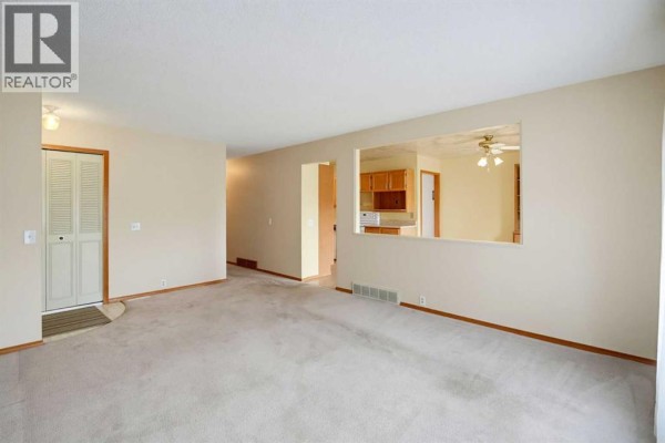 Interior view of the living room with carpet, beige walls, and an opening to the kitchen. - 8007 Huntington Street Ne, Calgary
