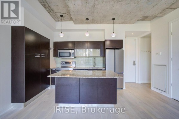 View of kitchen with stainless steel appliances, granite island, dark cabinets, and concrete ceiling. - 801 - 10 Morrison Street, Toronto