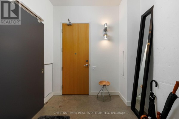 Apartment entryway with a wooden door, grey sliding closet door, tall mirror, and stool. - 801 - 155 Dalhousie Street, Toronto