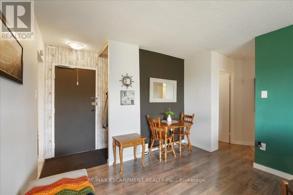 Living and dining area with a small wooden table, chairs, and dark accent wall. - 801 - 1966 Main Street W, Hamilton