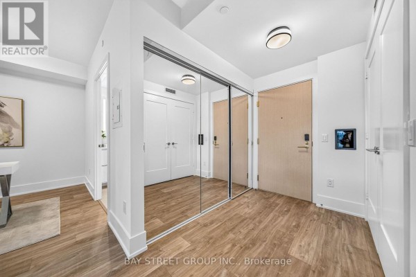 Hallway with wood-look floors, mirrored closet doors, and entry doors. - 801 - 480 Front Street W, Toronto