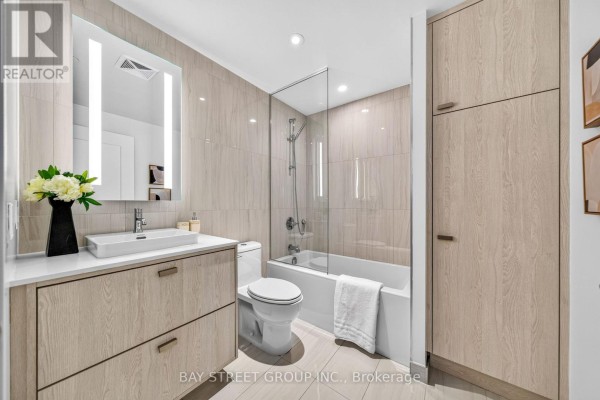 Bathroom with light wood vanity, toilet, bathtub, and tiled walls. - 801 - 480 Front Street W, Toronto