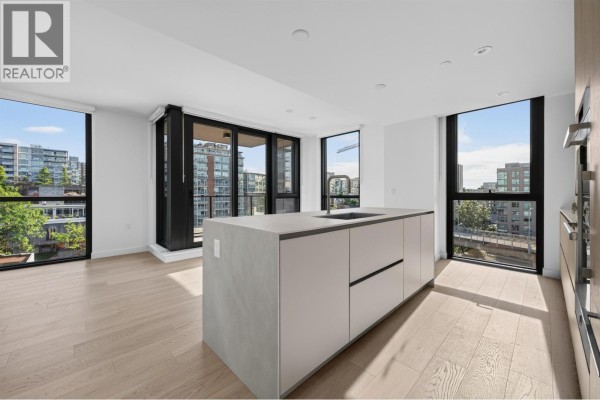 Open concept kitchen and living area with large windows, light wood floors, and a concrete island. - 801 1530 W 6th Avenue, Vancouver