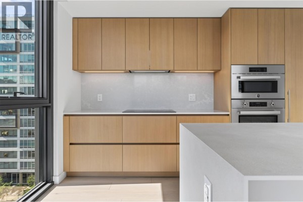 Close-up of modern kitchen cabinets, countertop, and stainless steel ovens with large windows nearby. - 801 1530 W 6th Avenue, Vancouver