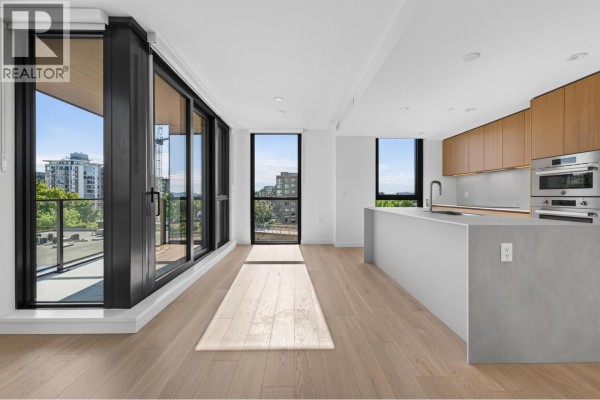Spacious living area with light wood floors, large windows, balcony access, and a modern kitchen island. - 801 1530 W 6th Avenue, Vancouver