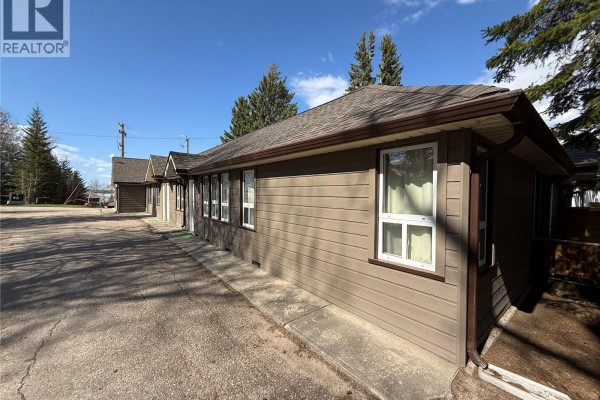 Side view of a two-story building with brown siding and large windows, surrounded by birch trees. - 801 Lakeview Drive, Prince Albert National Park