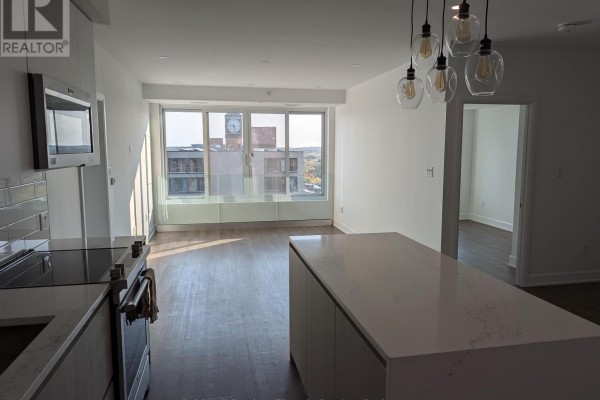 Open concept living area with kitchen island and large window. - 802 - 195 Hunter Street E, Peterborough