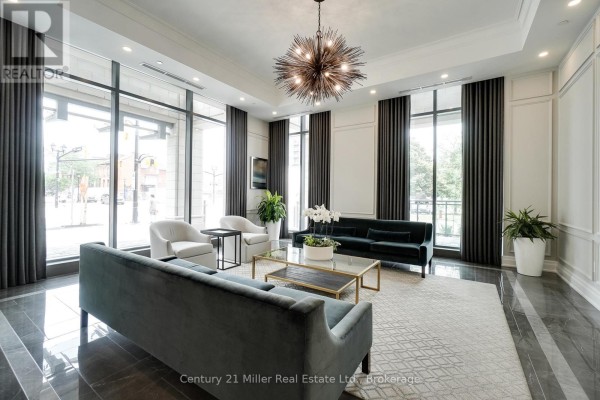 Luxurious lobby area with dark sofas, white armchairs, a glass coffee table, and a large chandelier. - 802 - 2060 Lakeshore Road, Burlington