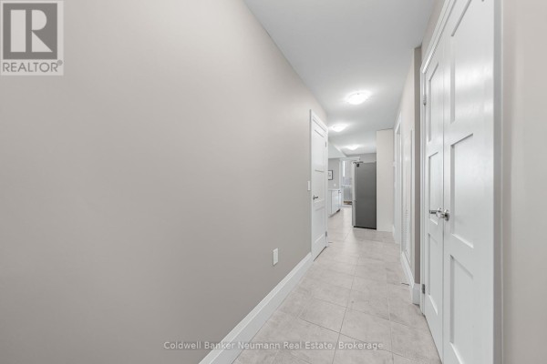 Interior hallway of apartment with tiled floor, white doors, and a glimpse of kitchen appliances. - 802 - 73 Arthur Street, Guelph