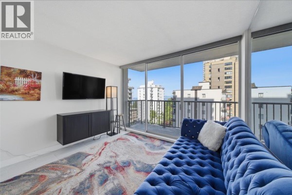 Living room with blue velvet sofa, television, and sliding glass doors to balcony. - 802 1251 Cardero Street, Vancouver