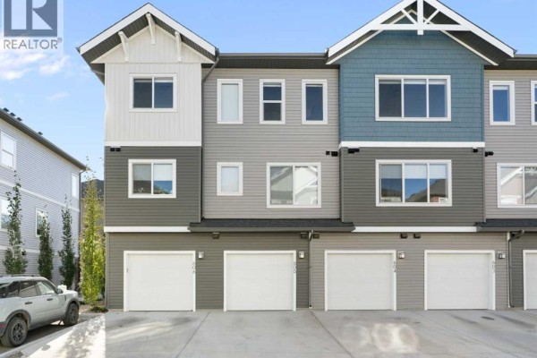Front exterior of townhouses with attached garages and multi-colored siding. - 803, 24 Rivercrest Drive, Cochrane