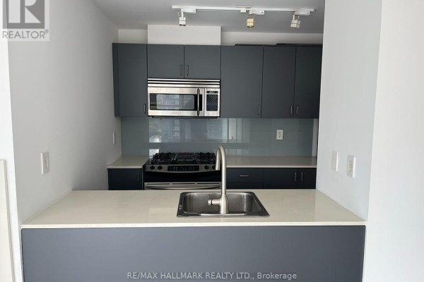 Close-up of a modern kitchen with grey cabinets, gas stove, and stainless steel sink. - 803 - 281 Mutual Street, Toronto