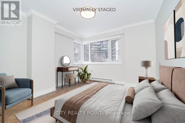 Bedroom with a bed, dresser, chair, and a large window overlooking city buildings. - 803 - 55 Isabella Street, Toronto
