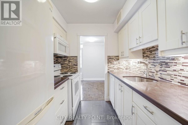 Galley kitchen with white cabinets, a white refrigerator, stove, microwave, and mosaic tile backsplash. - 803 - 55 Isabella Street, Toronto