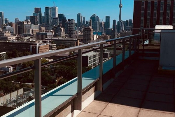 Tiled balcony with potted plants, chairs, and glass railings overlooking a cityscape. - 803 - 736 Spadina Avenue, Toronto