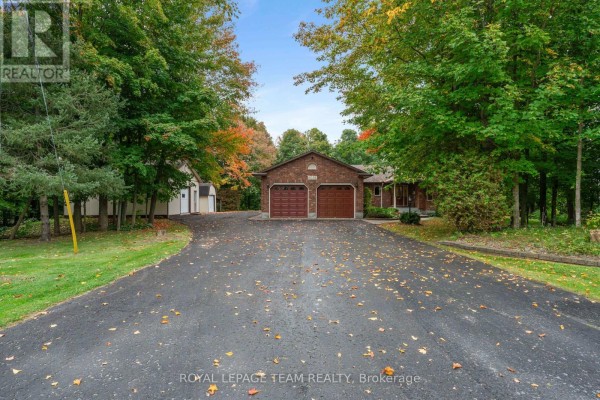 Long paved driveway leading to a brick house with a double garage and a detached garage. - 8036 Marionville Road, North Dundas