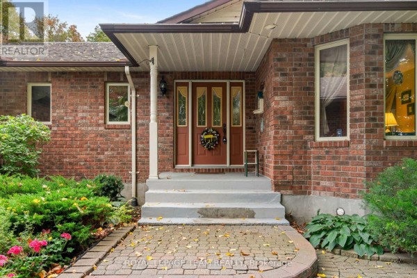 Entrance porch with a brick facade, grey steps, and a red front door with glass panels. - 8036 Marionville Road, North Dundas