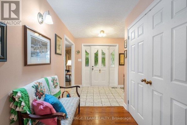 Interior hallway with pink walls, hardwood floor, a bench with colorful cushions, and double white doors. - 8036 Marionville Road, North Dundas