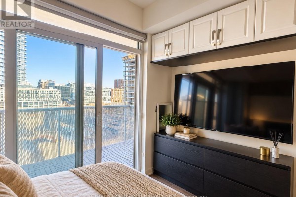 View from the bedroom looking towards a balcony with city views and a black dresser with mounted TV. - 804 - 20 Richardson Street, Toronto