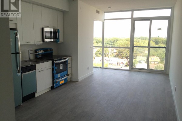 Empty apartment living area with white walls, wood-look flooring, and a stacked washer/dryer unit. - 804 - 2055 Danforth Avenue, Toronto
