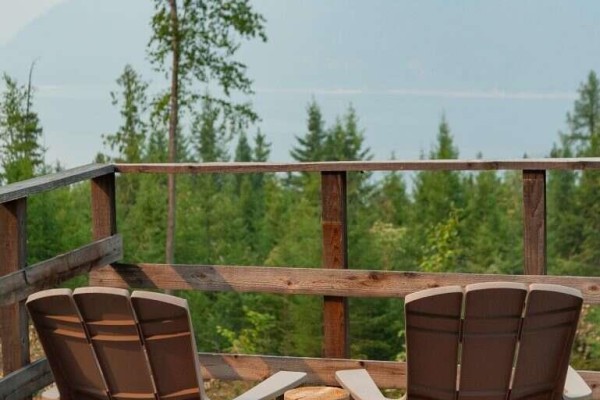 Wooden deck with two Adirondack chairs overlooking a dense evergreen forest. - 804 Applegrove Road, Fauquier