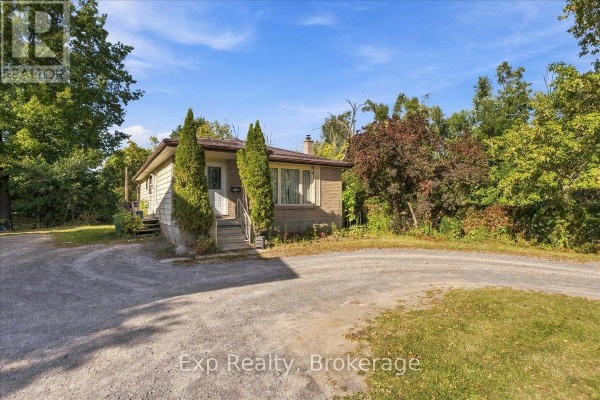 Wide view of the bungalow from the driveway, surrounded by trees and greenery. - 804 Sherbrooke Street, Peterborough