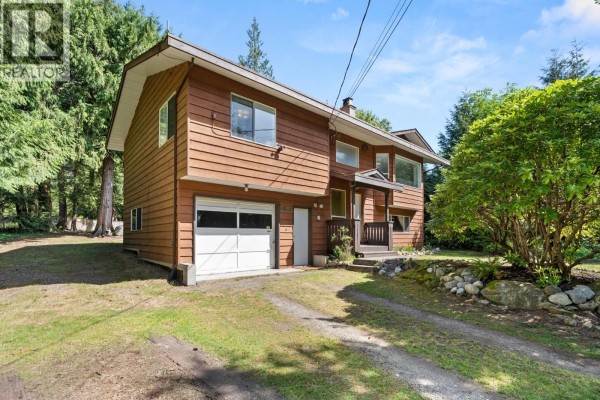 Side view of the house showing a white garage door and driveway on a grassy lot. - 8044 Dogwood Drive, Halfmoon Bay