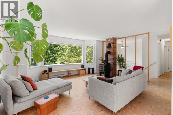 Living room featuring sofas, a wood-burning stove, and a large window with a forest view. - 8044 Dogwood Drive, Halfmoon Bay