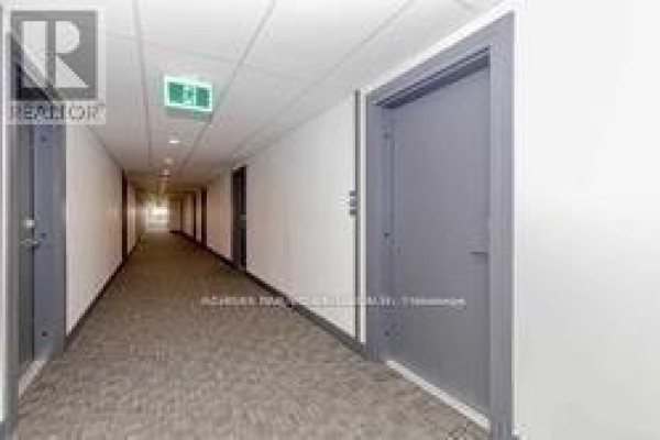 Long apartment hallway with grey doors, white walls, and patterned carpet. - 805 - 1 Wellington Street, Brantford